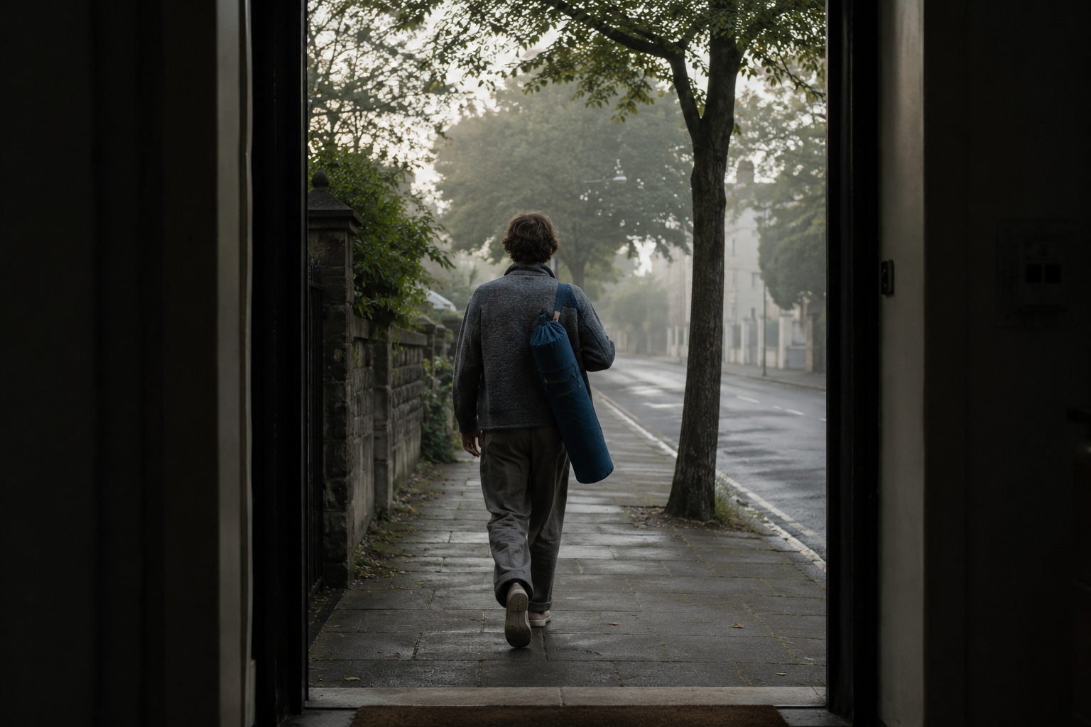 A person leaving for practice, mat carried under the arm, on a misty street.